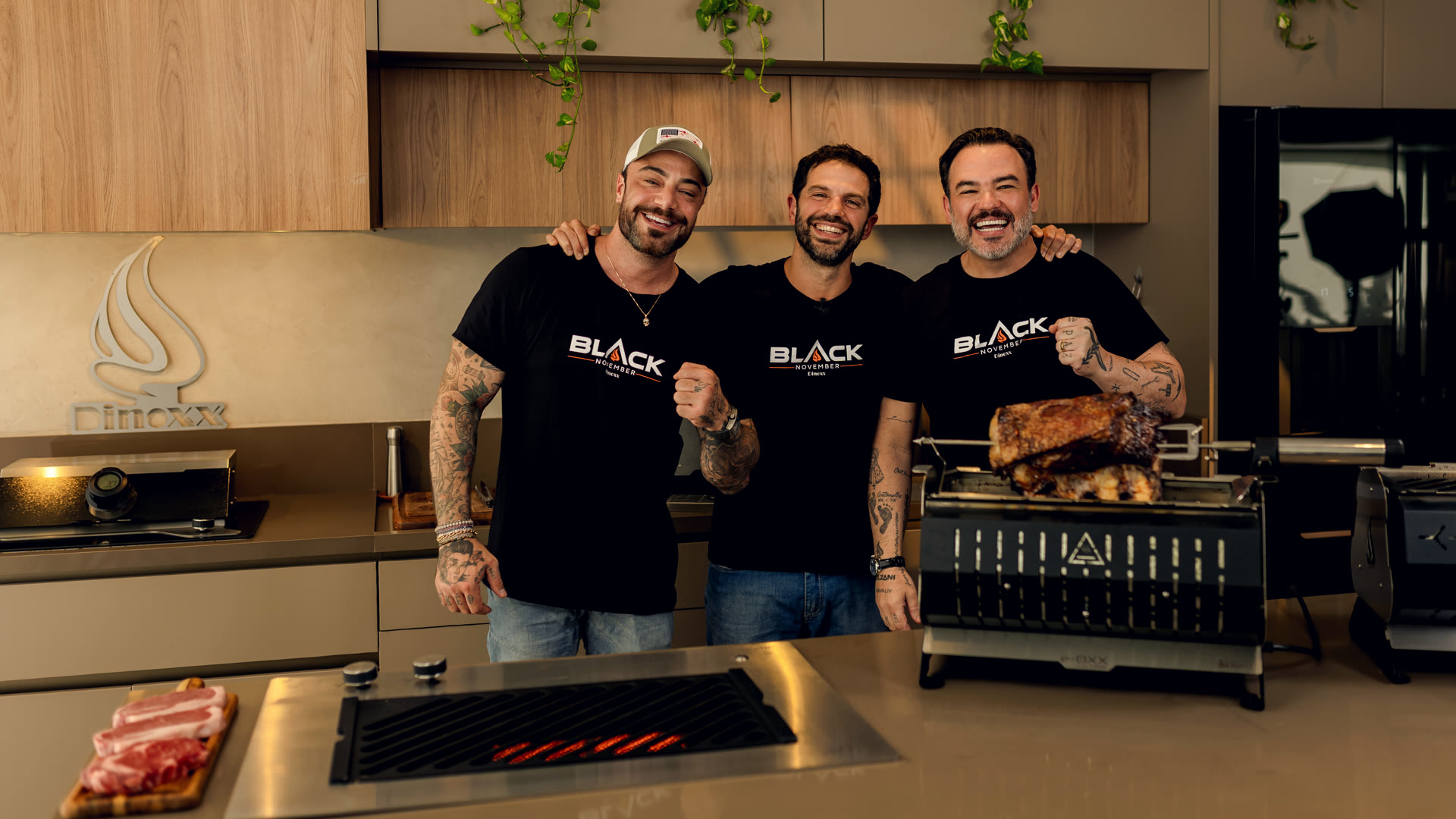Felipe Titto, Duda Nagle e Rick Bolzani na cozinha Dinoxx, ao lado de uma churrasqueira elétrica com costela no espeto giratório.